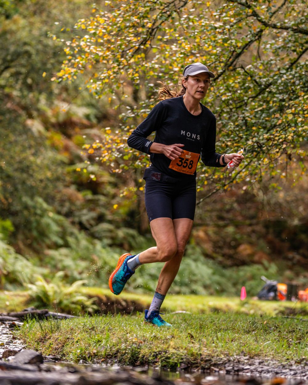 Trail runner in black outfit jumping over creek in autumn forest setting.