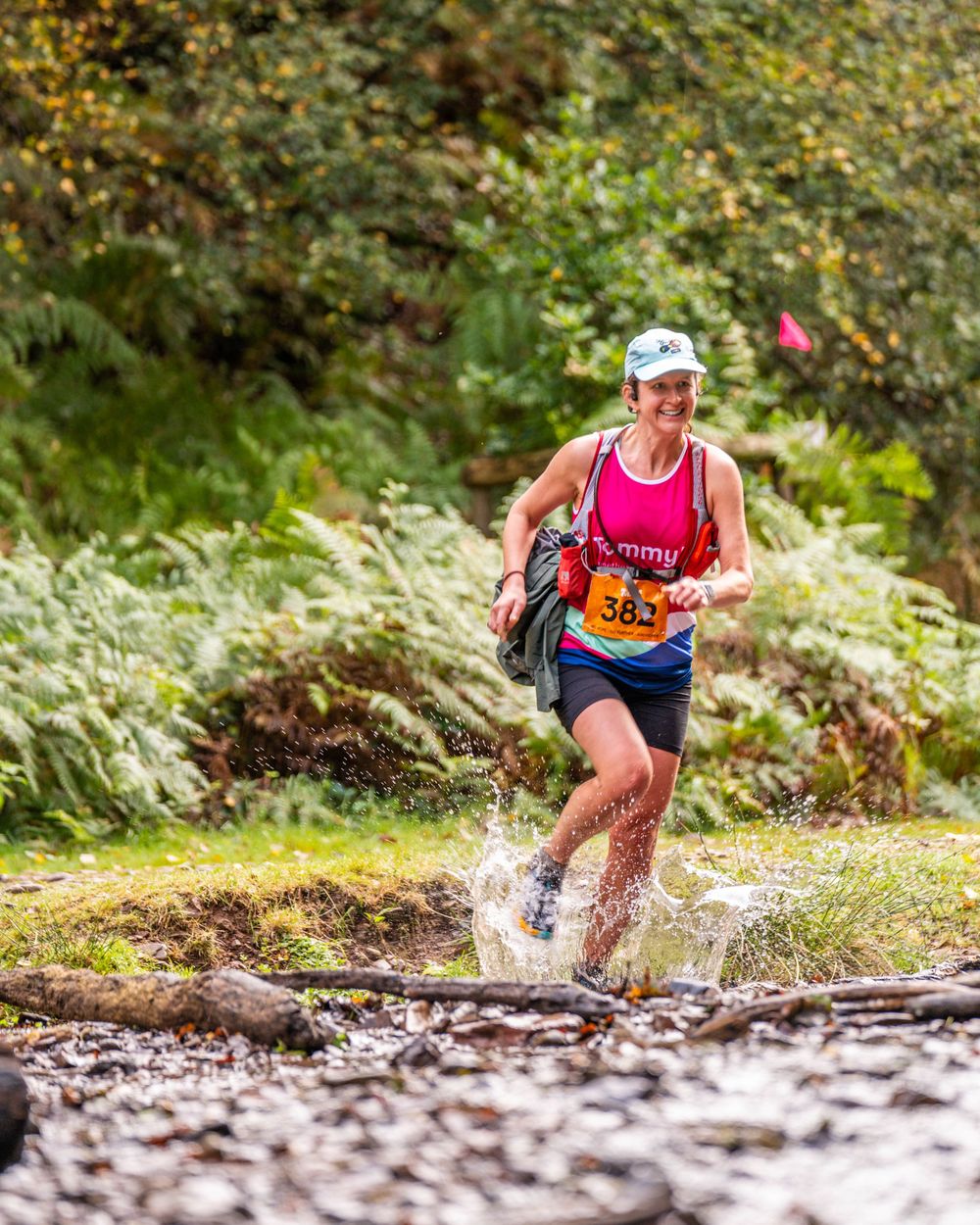 Runner splashing through muddy water crossing on forest trail course.