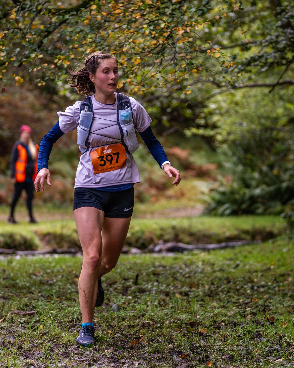 Trail runner navigating wooded course with race bib during competition.