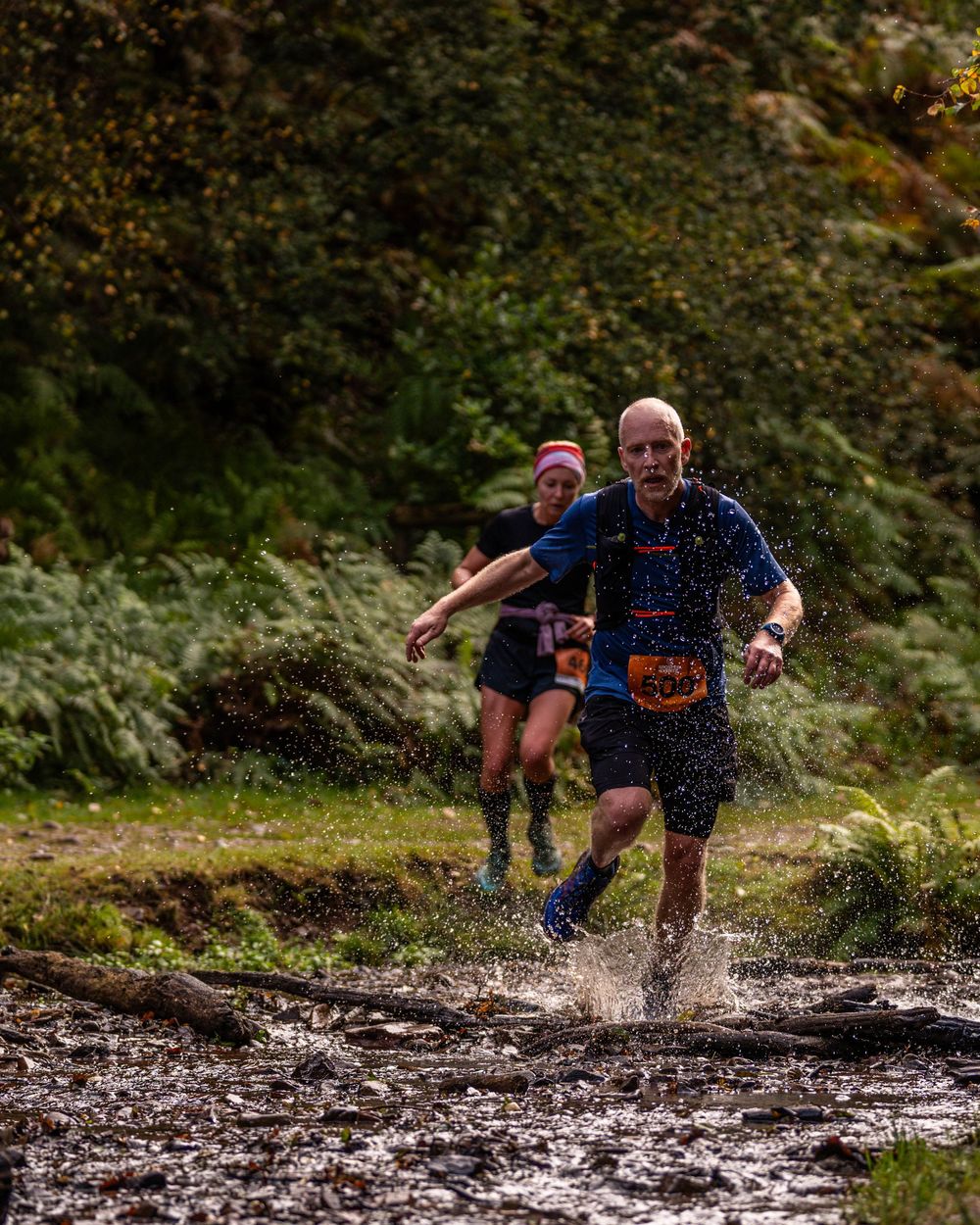 Trail runners splash through muddy terrain during an autumn trail race in a lush forest setting.