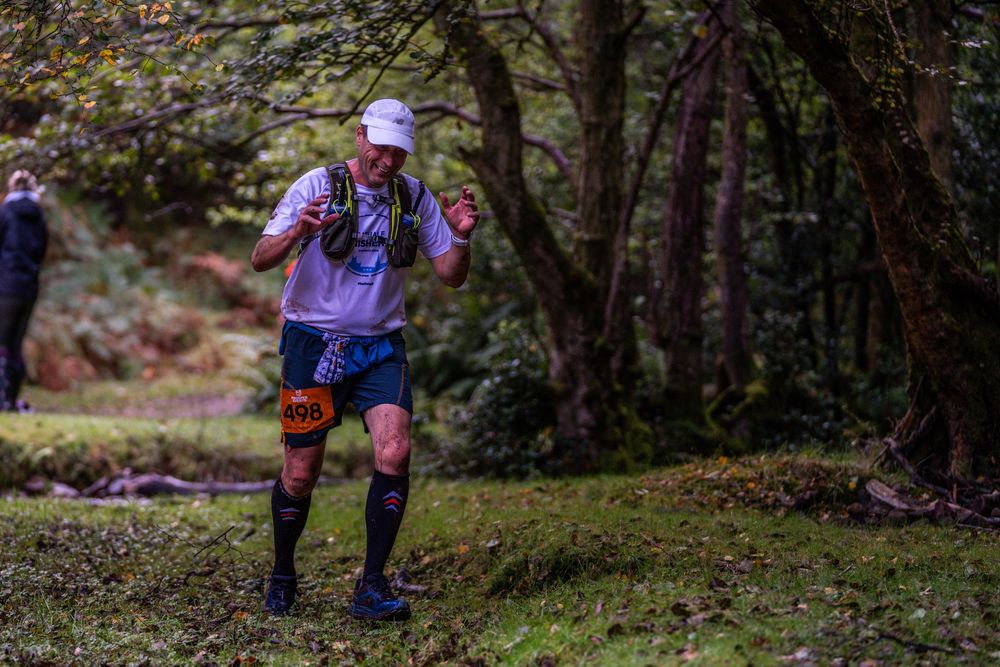 Trail runner in purple shirt navigates wooded course during autumn race.