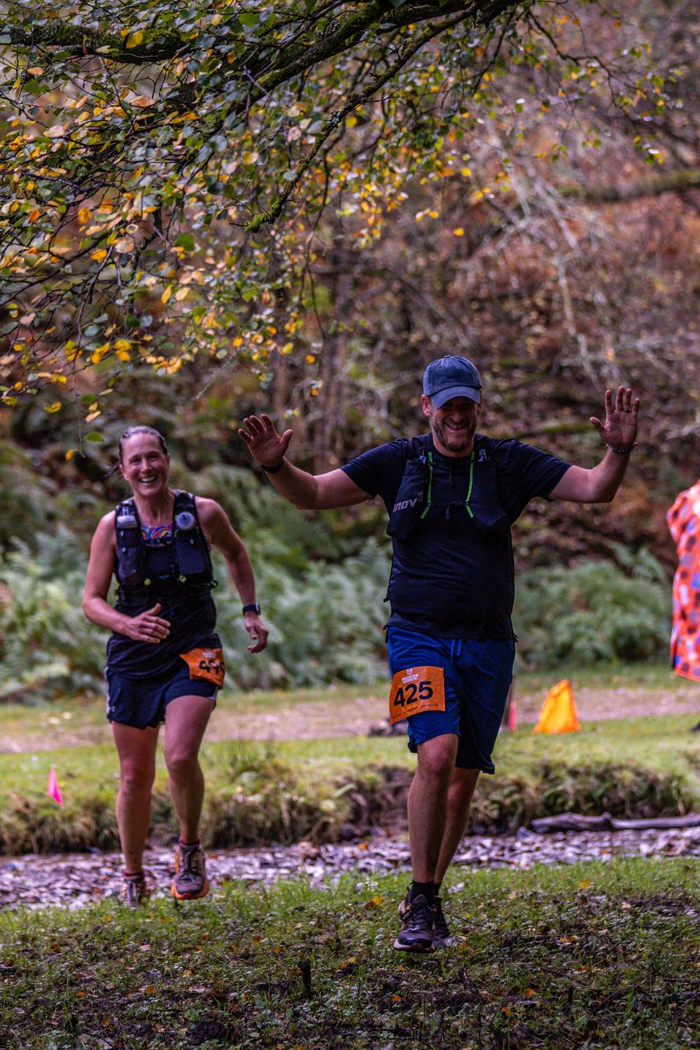 Enthusiastic trail runners celebrate while crossing muddy terrain during forest race.