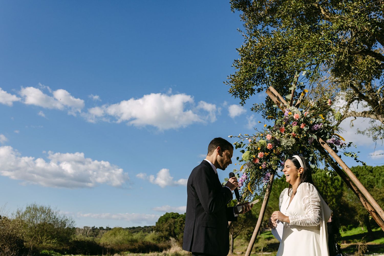 Bride and groom exchanging vows during ceremony by the lake at herdade do moinho novo, in setubal
