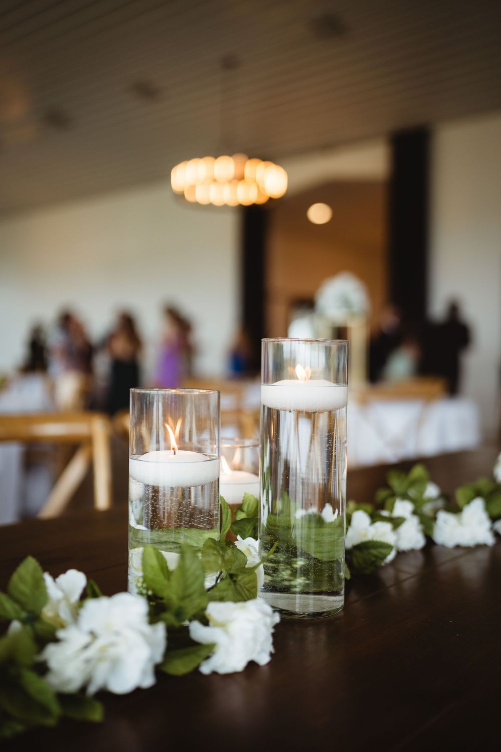 White floral centerpiece arrangements with glass candle holders line an elegant dining table.