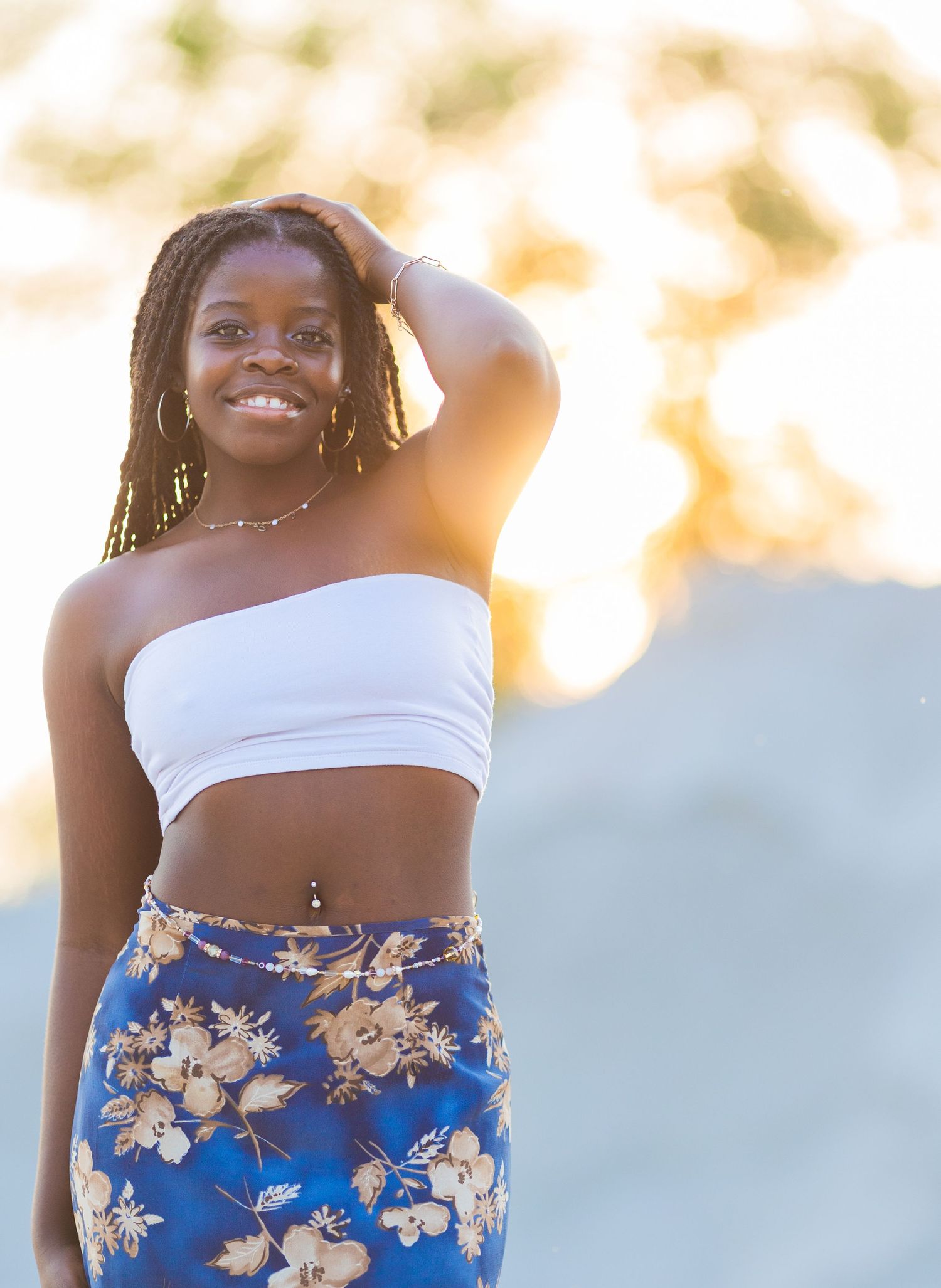 A joyful figure in a white crop top and floral print skirt poses outdoors during golden hour lighting.