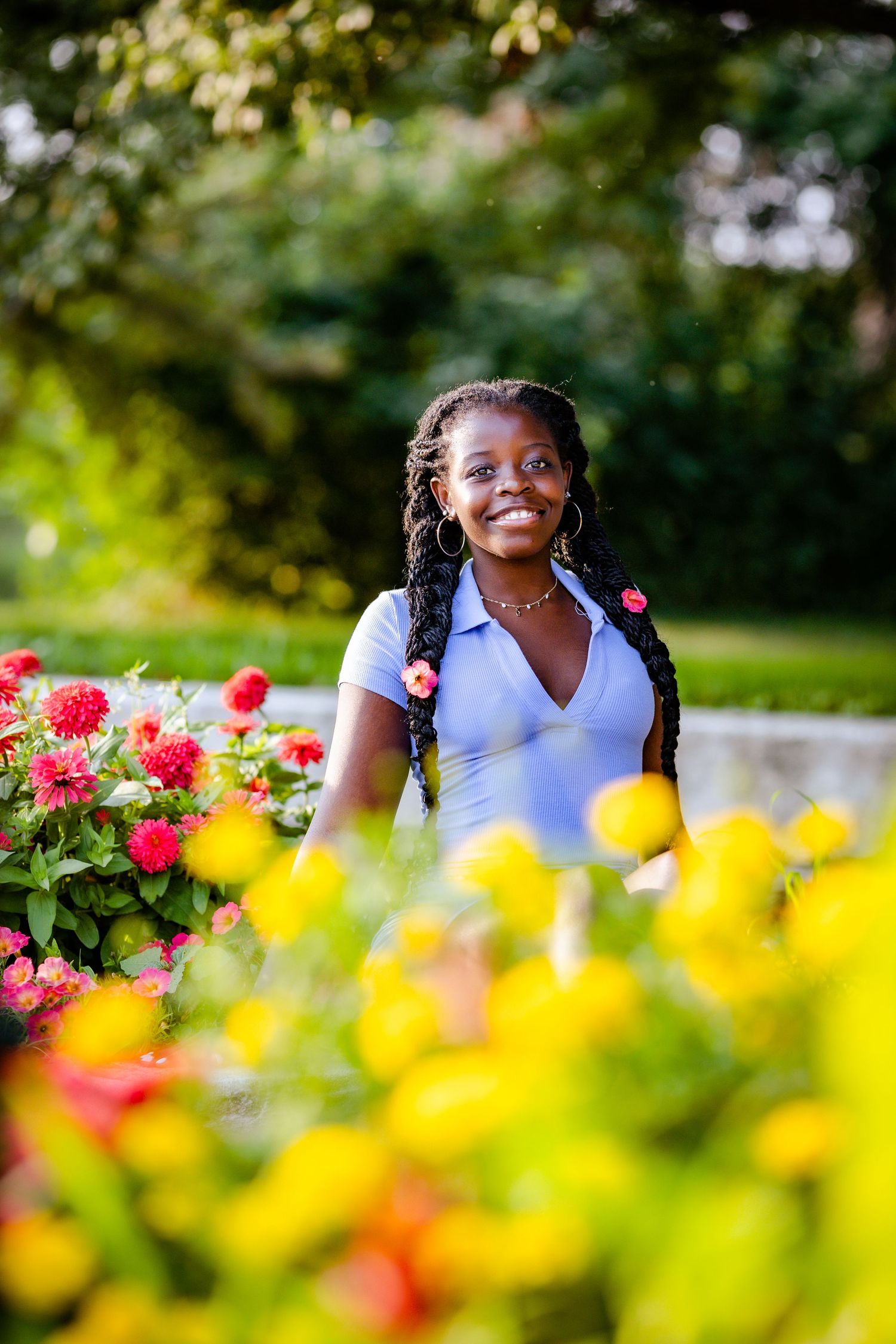 A joyful portrait in a garden with bright red and yellow flowers blooming in the foreground on a sunny day.