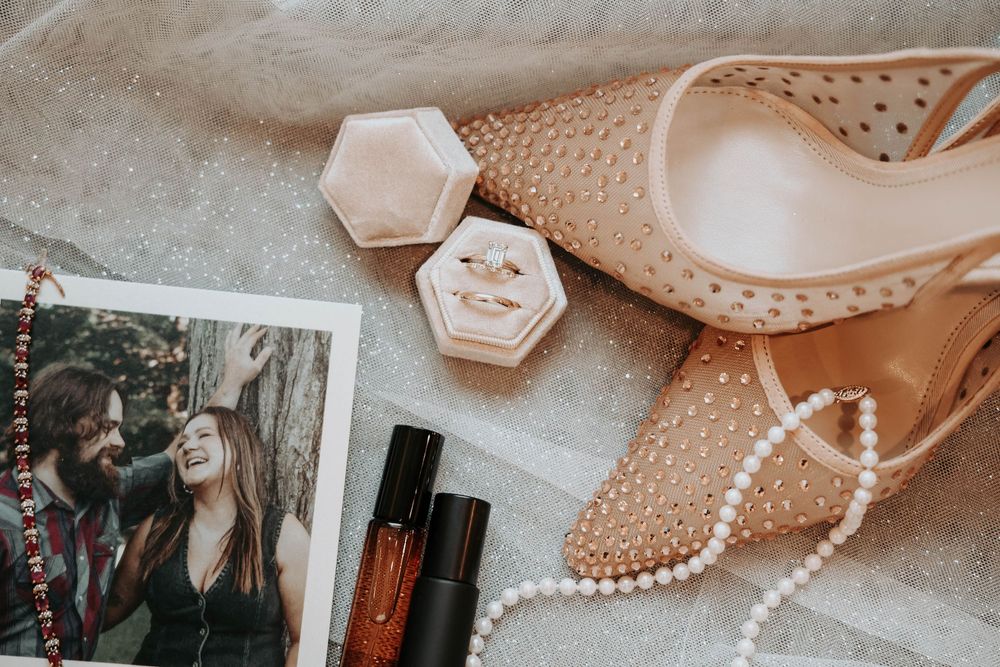 Flatlay photography of wedding accessories including vintage shoes, pearl necklace, and makeup items in soft beige tones.