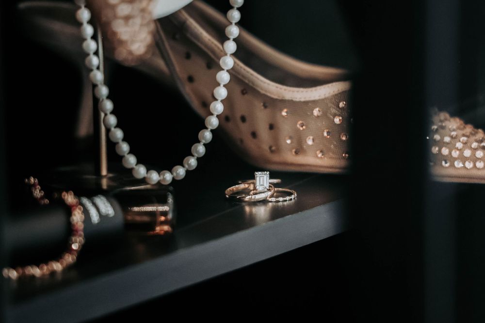 A close-up display of luxury jewelry including pearl necklaces and sparkling rings arranged on a dark shelf.