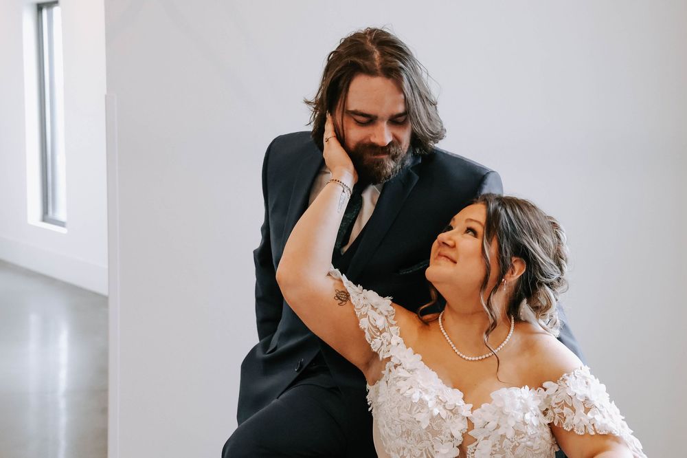 A couple shares an intimate moment together while dressed in formal wedding attire indoors.