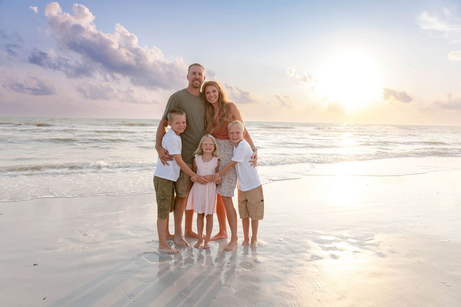 Family beach photography session at sunset with waves and soft lighting.