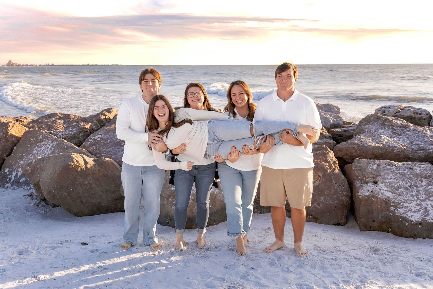 Extended family portrait on beach with rocks and waves during golden hour lighting.