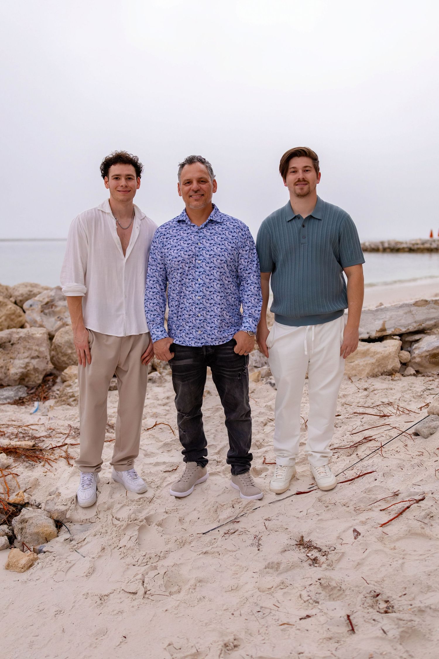 Group portrait on coastal rocks wearing coordinated neutral colored outfits against cloudy sky.