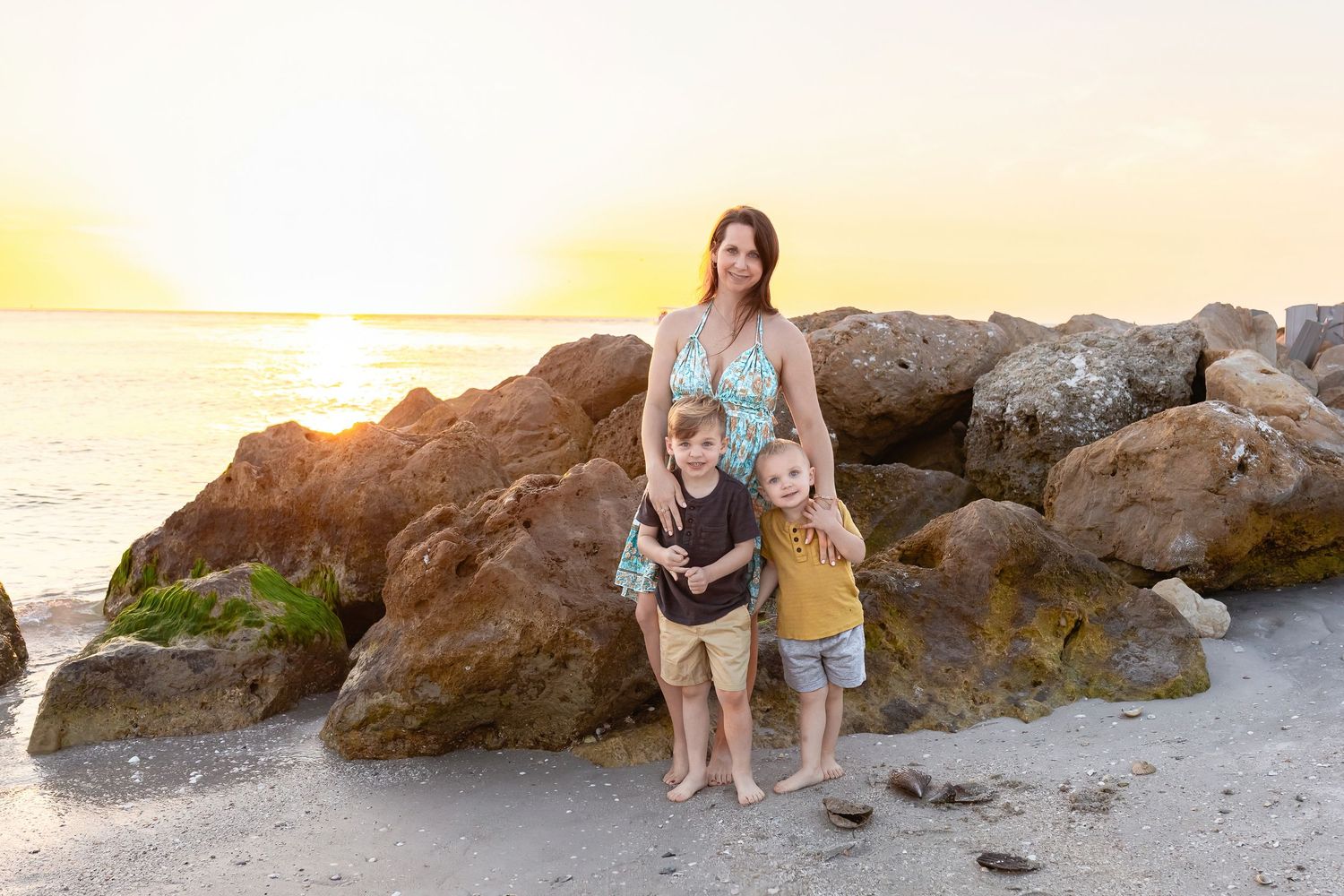 Family portrait session on rocky beach during golden hour with ocean waves in background.