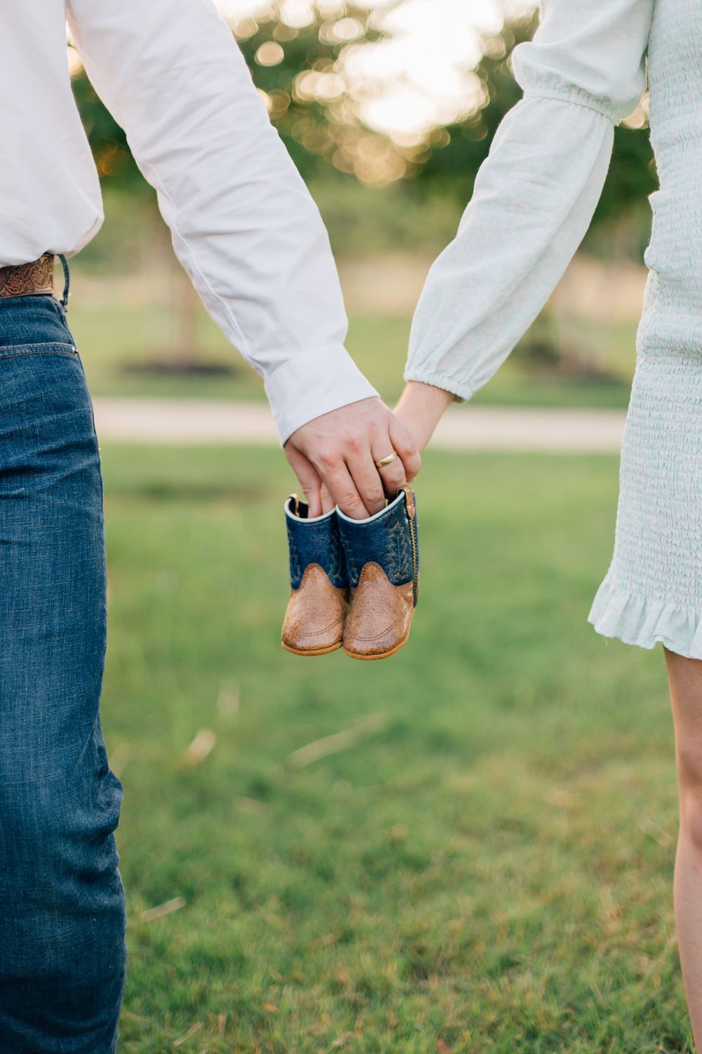 A couple holding a tiny pair of baby shoes together against a sunny outdoor background.