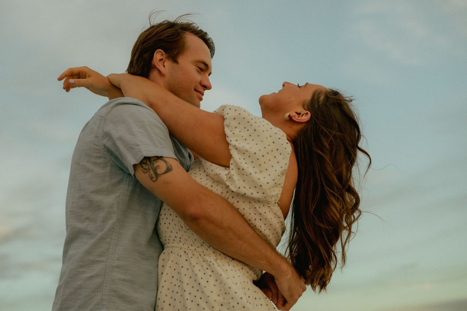 Romantic golden hour couples session in Florida — candid moment of laughter and embrace under a pastel sunset sky.