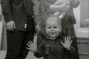 Black and white family photography in Hamilton — toddler smiling with raised hands during a candid home session.