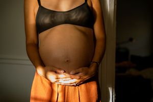 Hamilton maternity photography — moody indoor portrait of a pregnant woman cradling her belly in warm light.