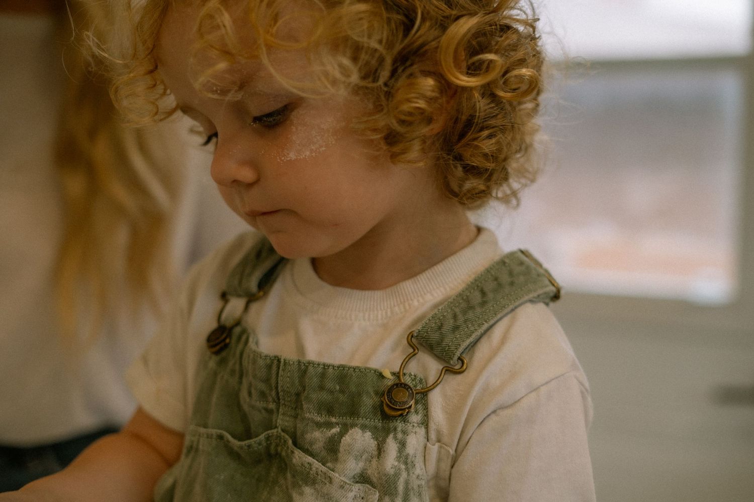 Candid child portrait at home — lifestyle family photography in Hamilton featuring a toddler in overalls and natural light.