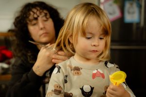 In-home documentary photography in Hamilton — child getting a first haircut while holding a toy during a candid family session.