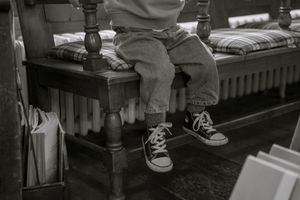 Black and white detail from an in-home family photo session in Hamilton — child's feet in Converse sneakers on a wooden bench.