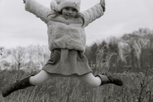 Joyful winter family photography in Hamilton — child jumping midair in cozy outerwear during a black and white outdoor session.