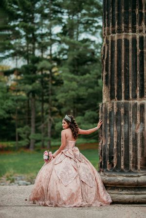 An elegant pink ballgown photographed against classical stone pillars in a garden setting.