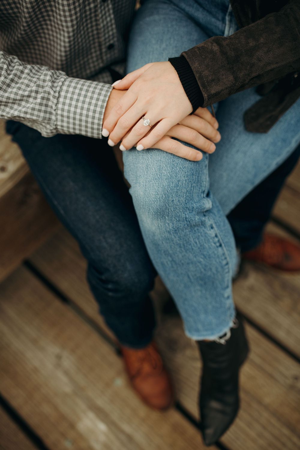 Close-up view of two intertwined hands resting on denim-clad knees, with plaid and suede sleeves visible.