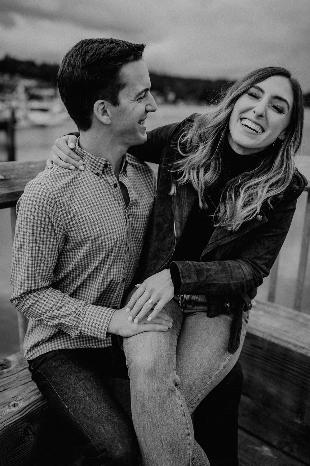 A happy couple sharing a candid laughing moment together on a dock in black and white photography.