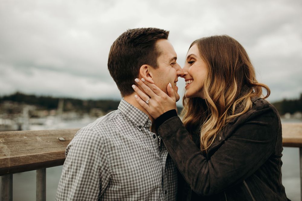 A romantic couple sharing an intimate moment on a deck overlooking a marina on a cloudy day.