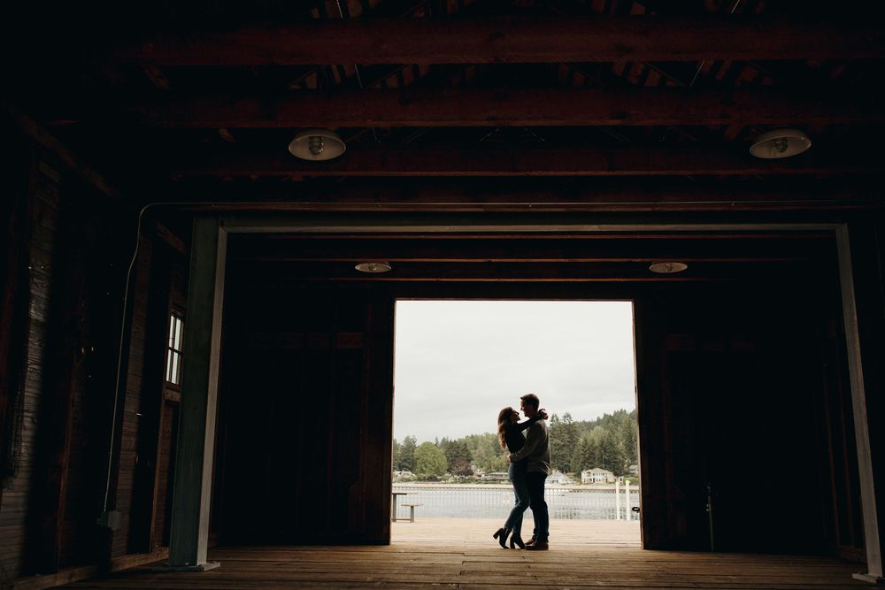 Silhouetted figures embrace in a doorway overlooking a waterfront view on an overcast day.