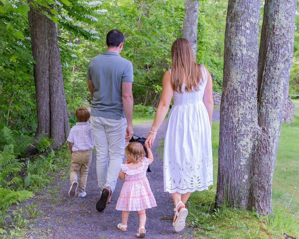 Family taking a peaceful walk together on a wooded trail with tall trees on a summer day during a family photo session in Sudbury, MA