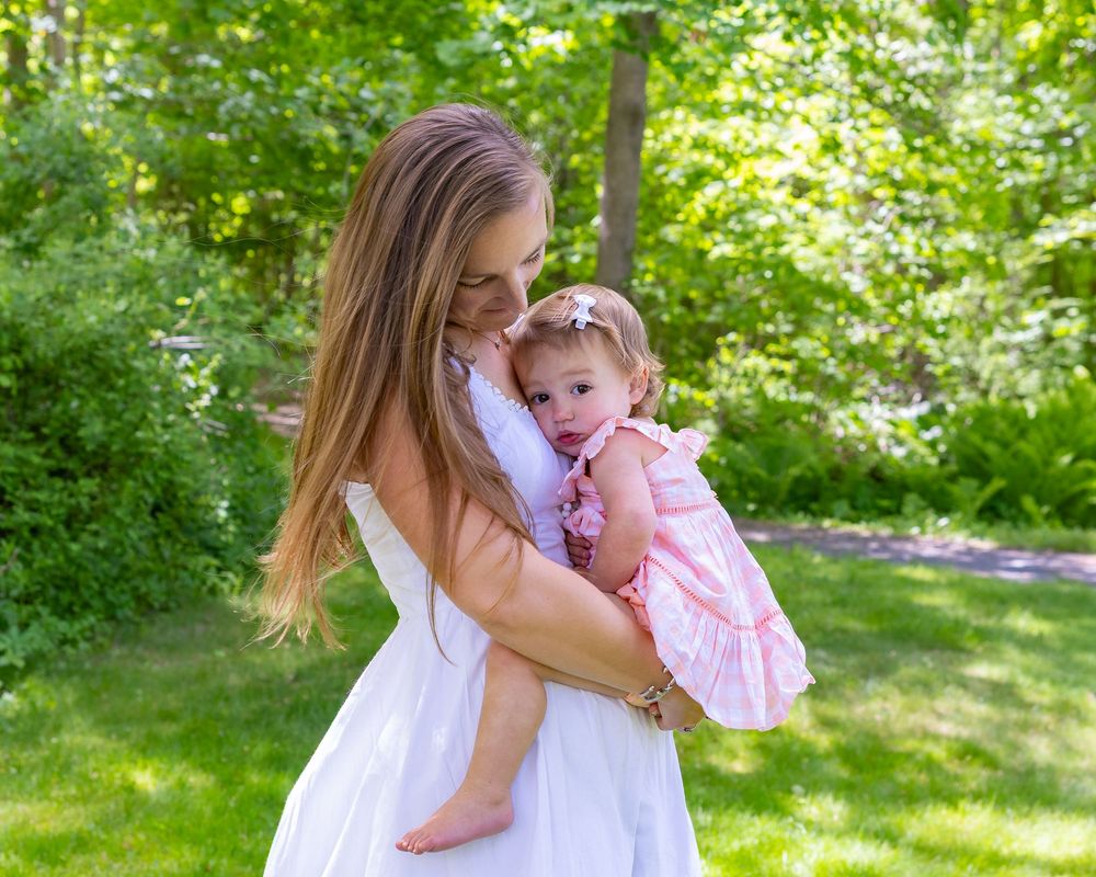 Heartwarming embrace between parent and baby in pink dress against leafy green background during a family photo session in Sudbury, MA
