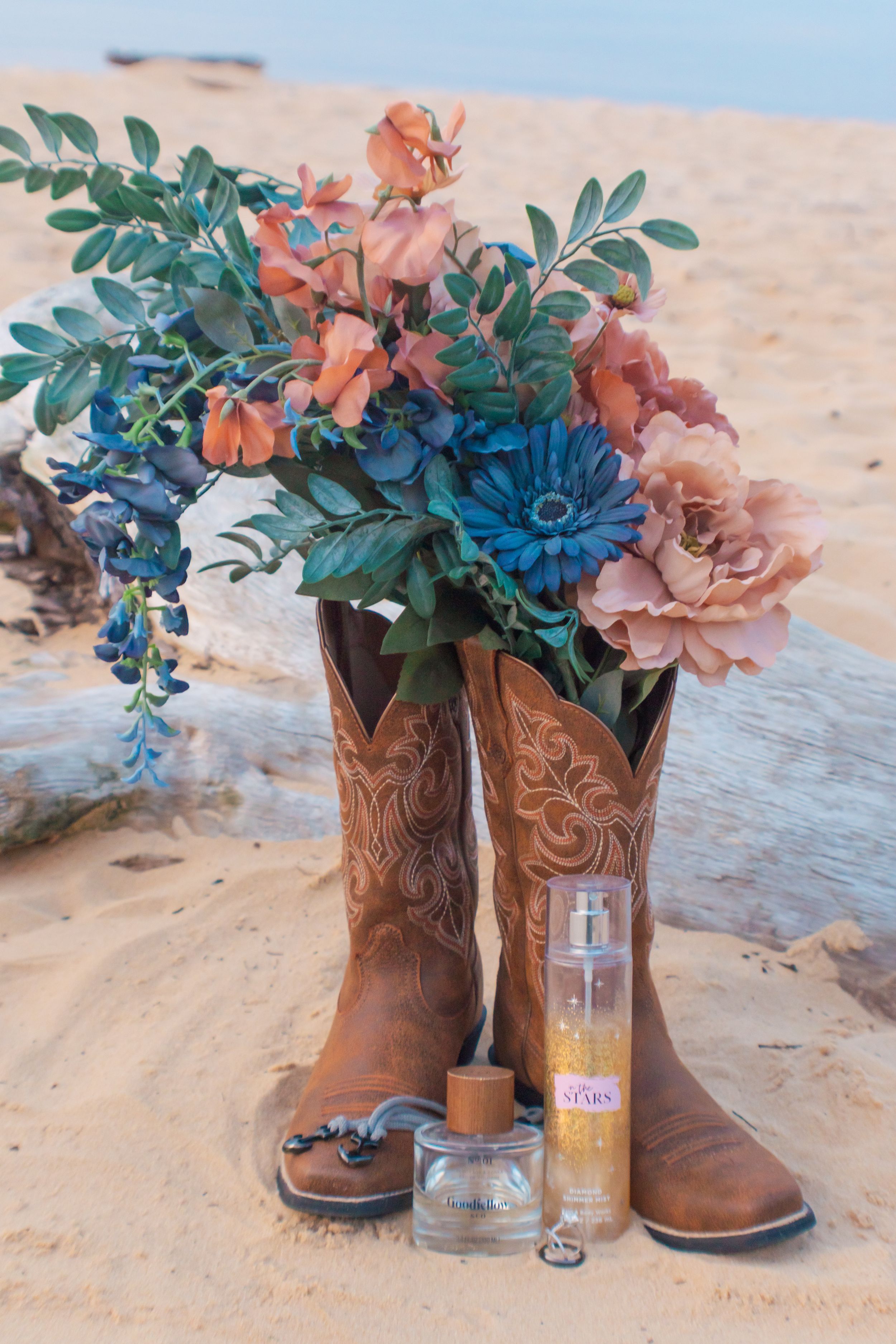 Brown leather cowboy boots decorated with flowers serve as rustic vases for colorful floral arrangements on a wooden surface.