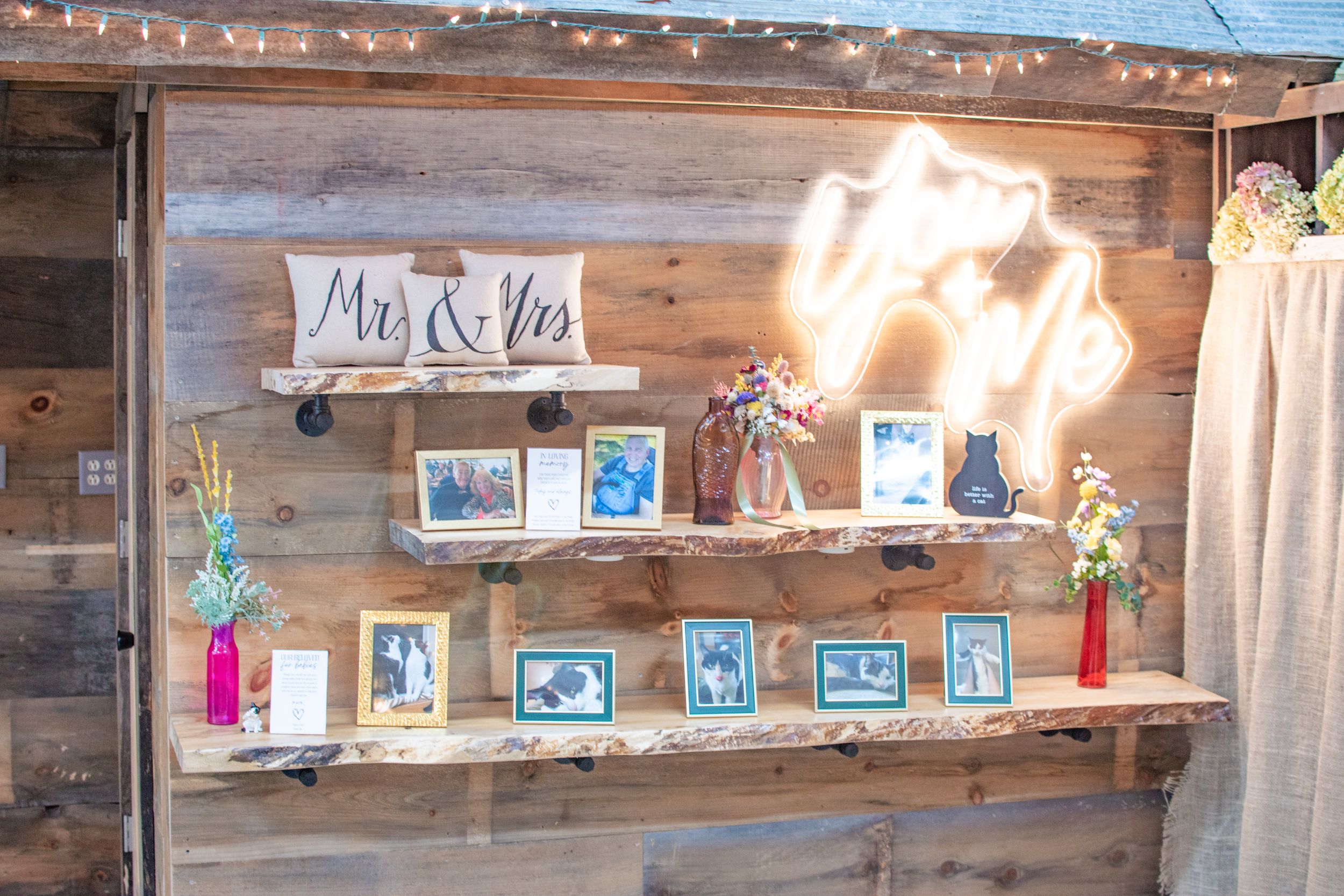A rustic wooden shelf with neon sign and framed photos creates a wedding memory display.