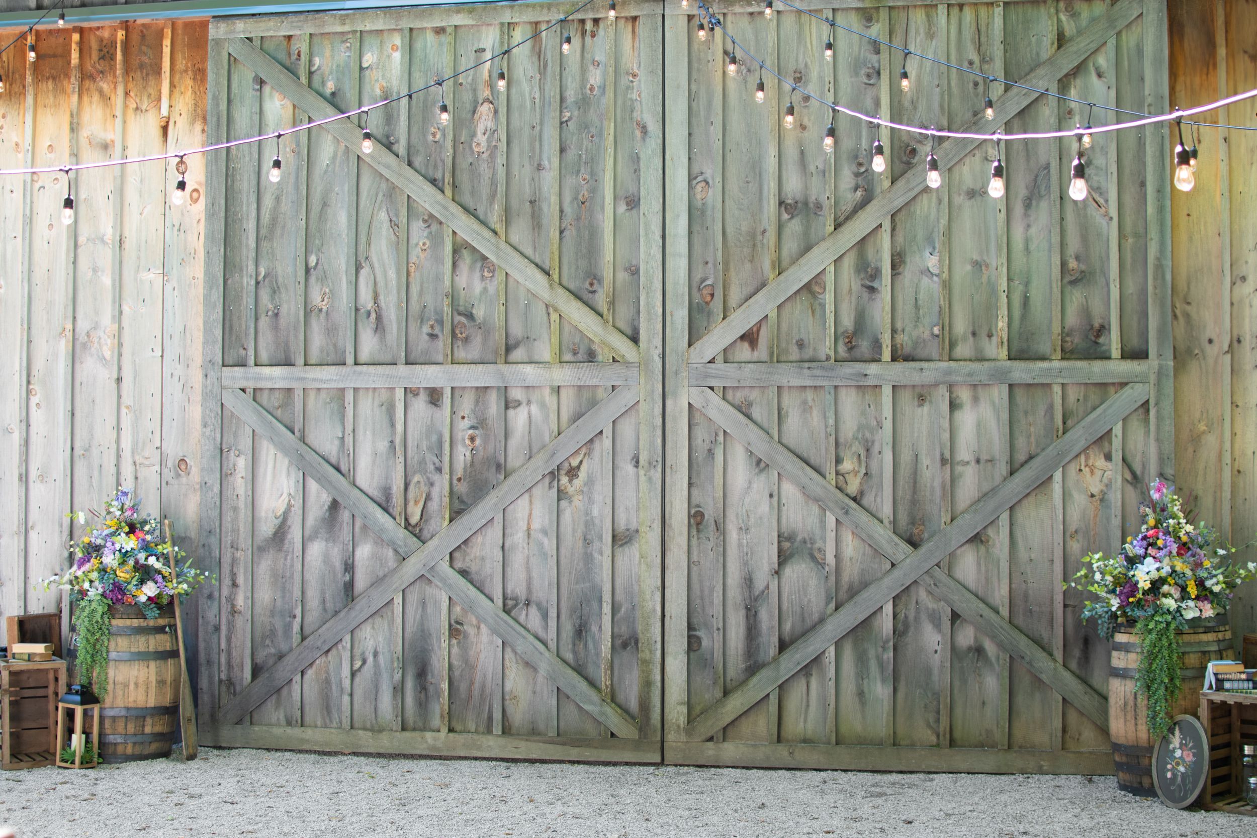 A rustic barn door backdrop decorated with string lights and floral arrangements.