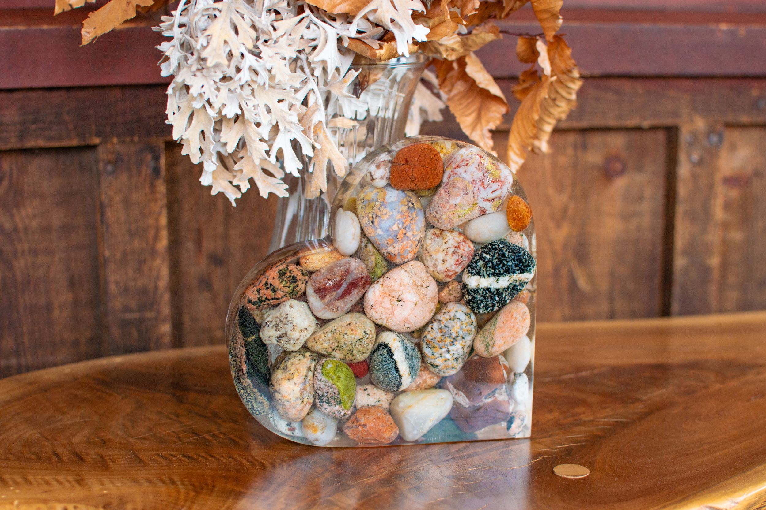 A glass vase filled with colorful stones and dried flowers on a wooden table.