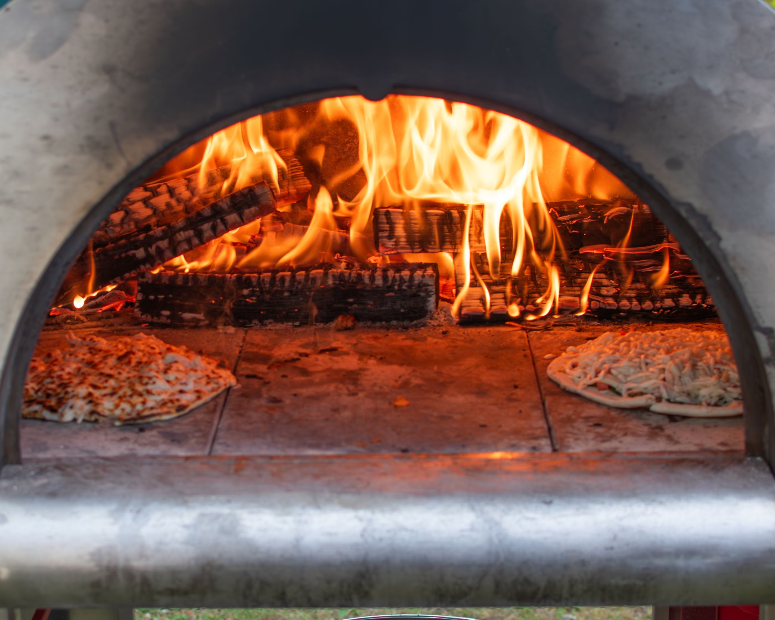 Close-up of burning wood logs in a brick pizza oven with bright orange flames.