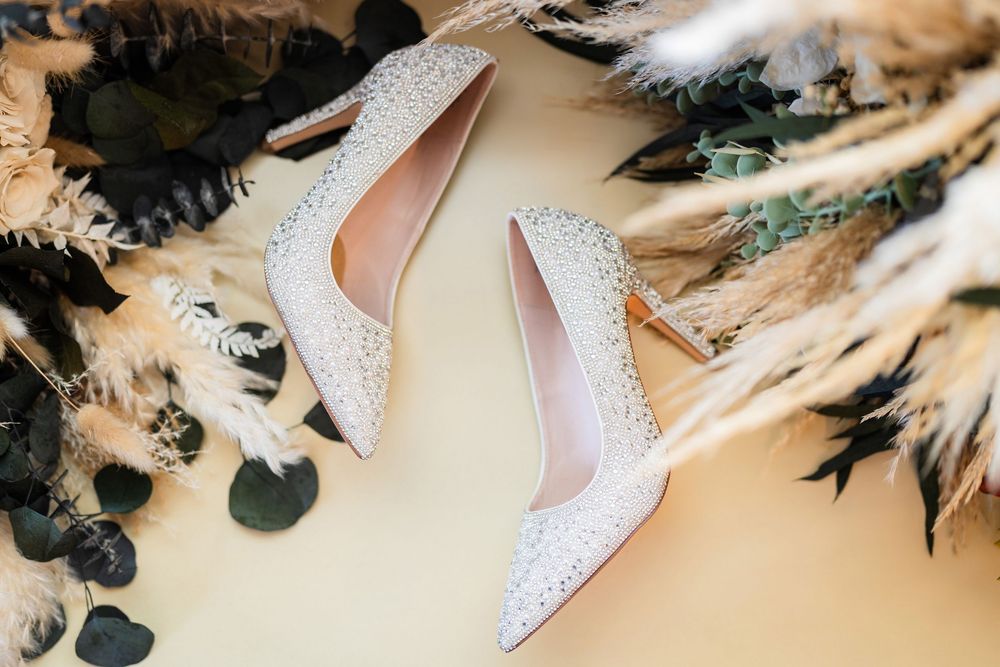 Elegant white glittery bridal heels positioned on a light-colored surface with feather decorations.