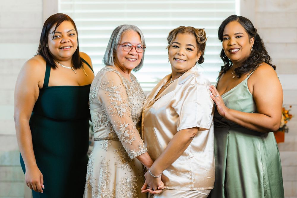 Four people pose together while wearing elegant evening dresses in dark and neutral tones.
