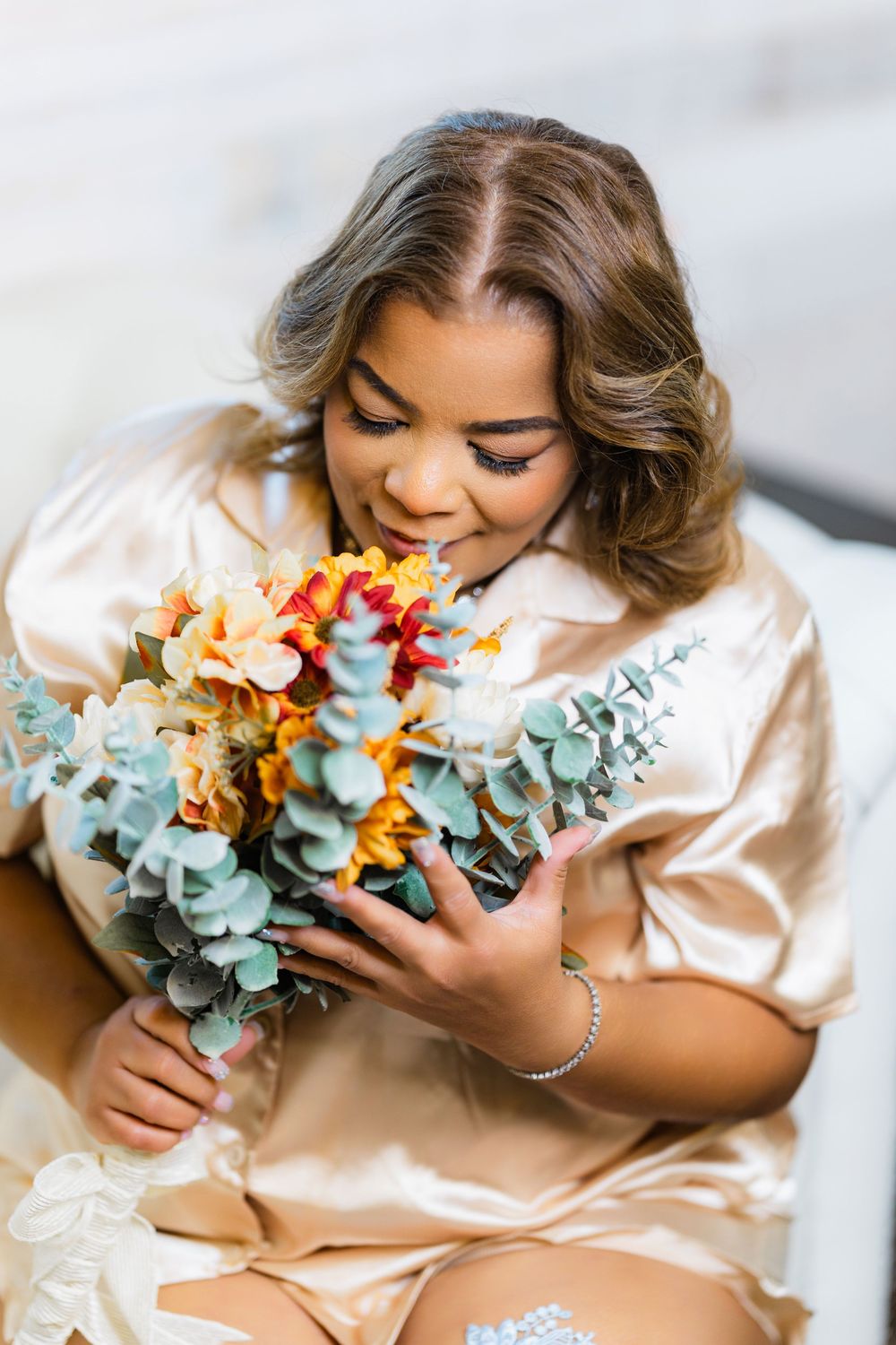 Person in silk robe smelling colorful fall wedding bouquet with eucalyptus and orange flowers.