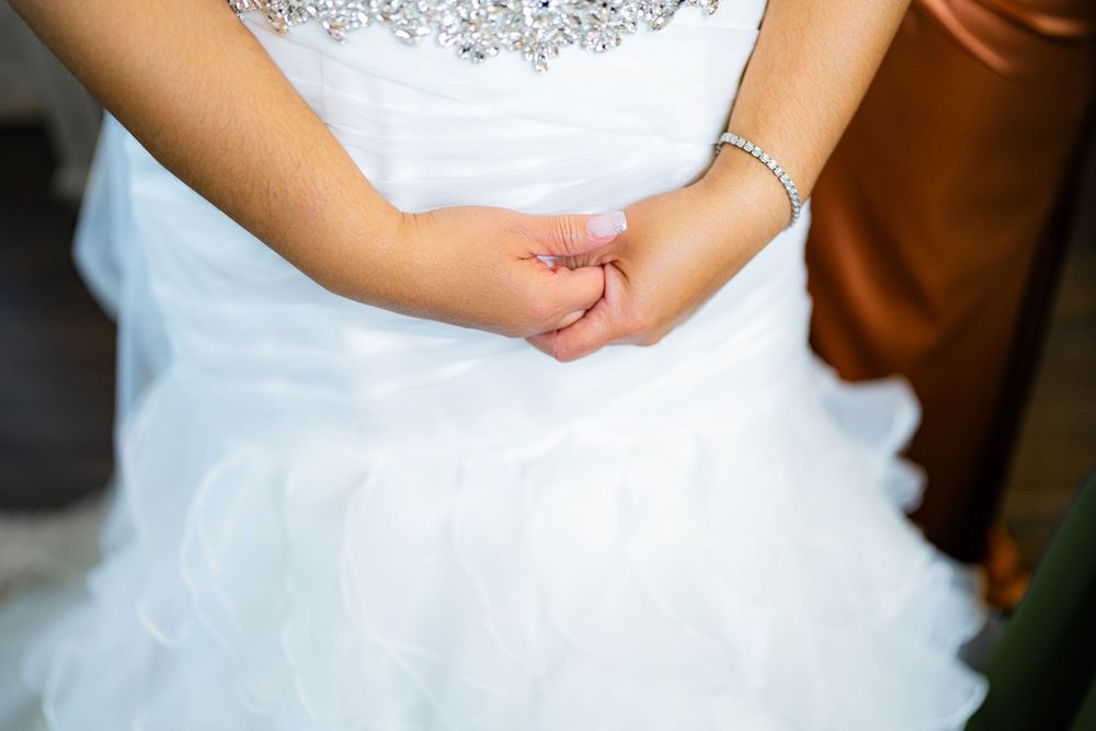 Close-up of bride's hands in white wedding dress showing delicate bracelet detail.