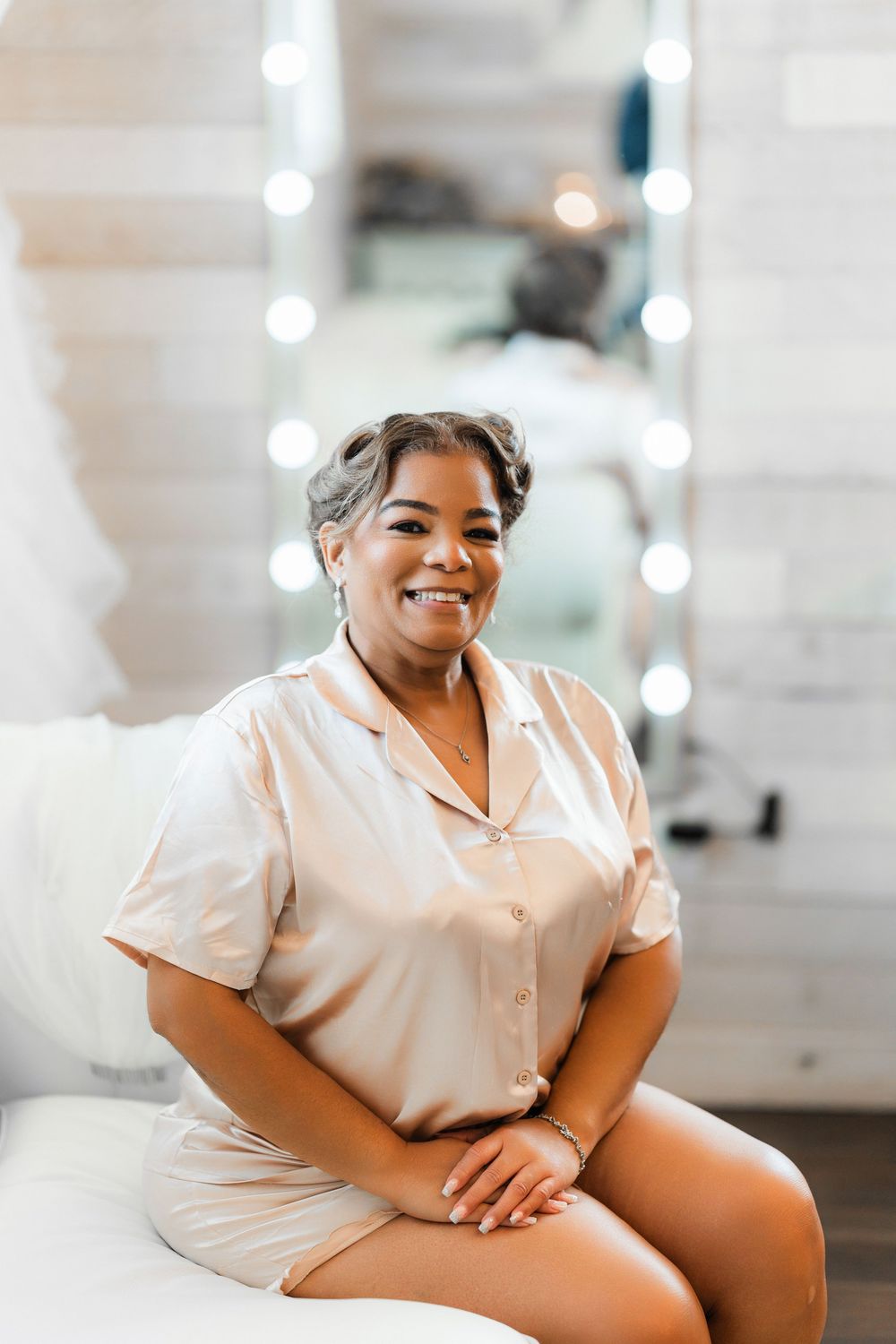 Person in light beige attire sitting on white furniture with twinkle lights in background.