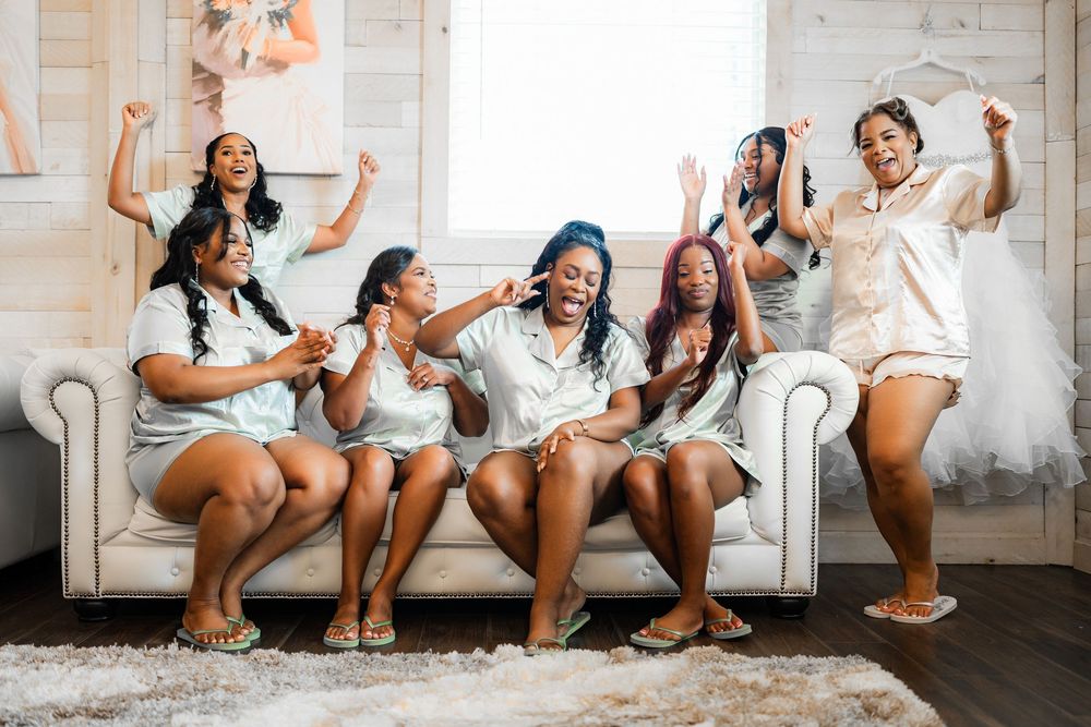 Group of friends in white outfits celebrate joyfully on a white couch in a bright studio setting.