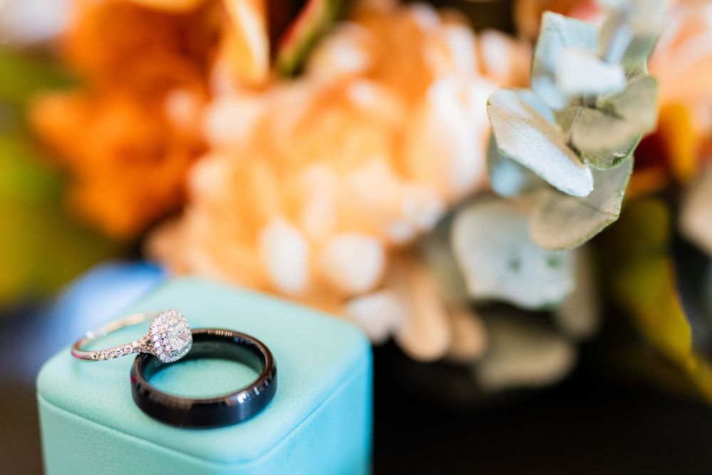 A black engagement ring with a diamond sits atop a turquoise jewelry box with peach flowers in the background.