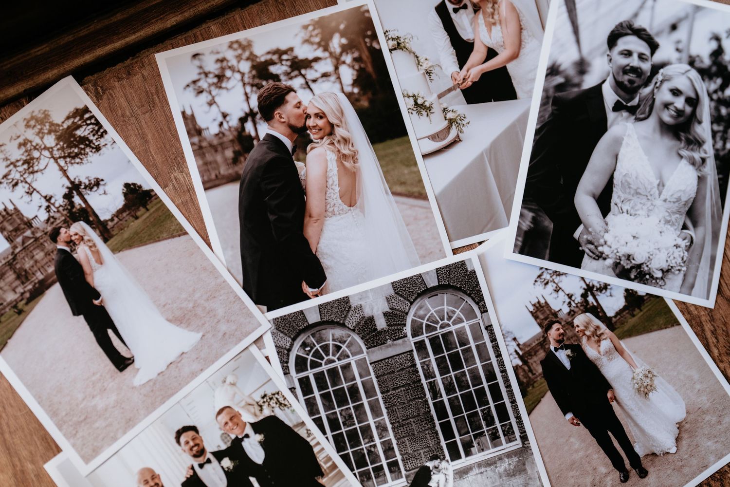 A collection of wedding photographs in black and white and sepia tones scattered on a wooden surface.