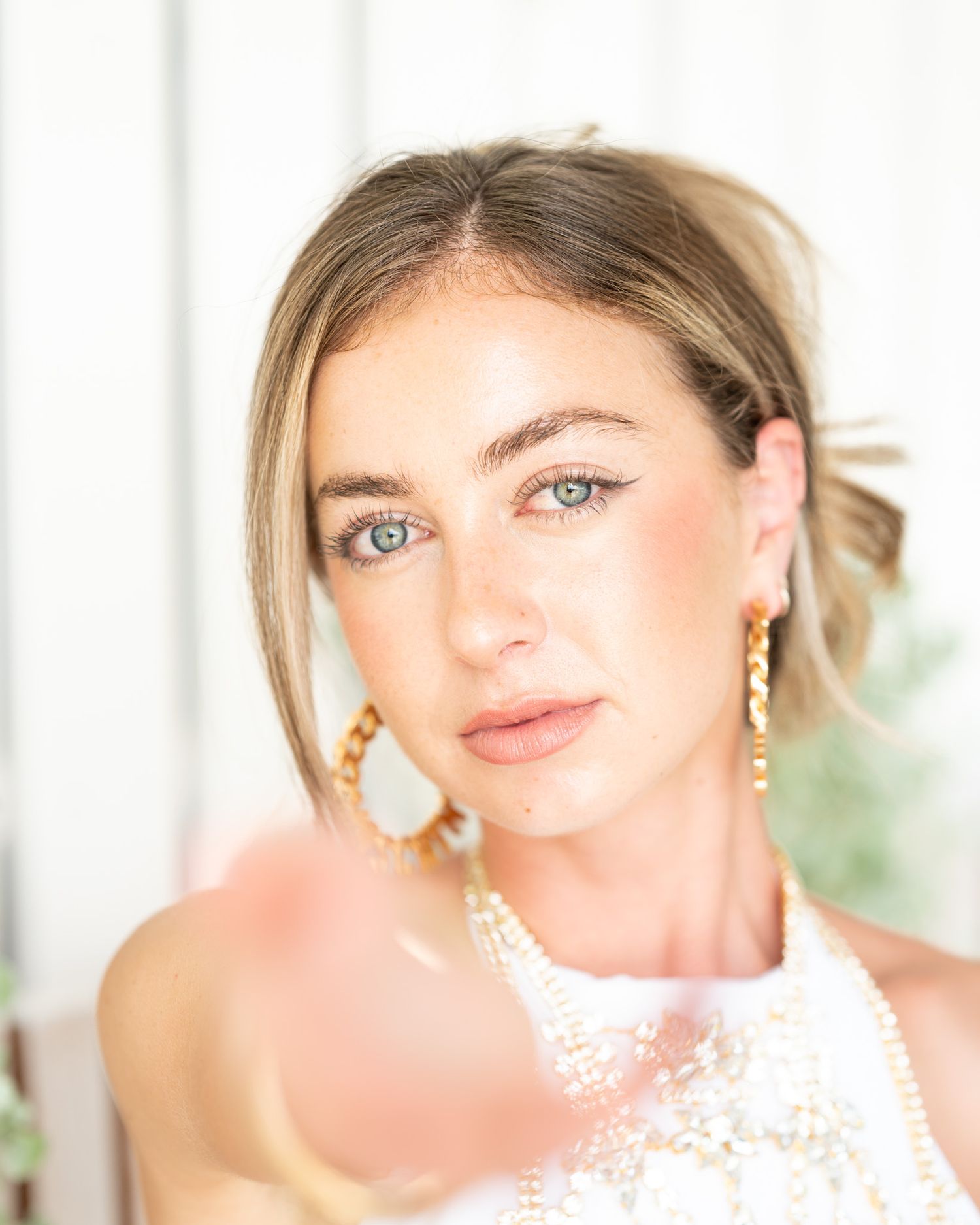 Portrait showcasing elegant bridal makeup, pearl jewelry and blonde updo against white background.