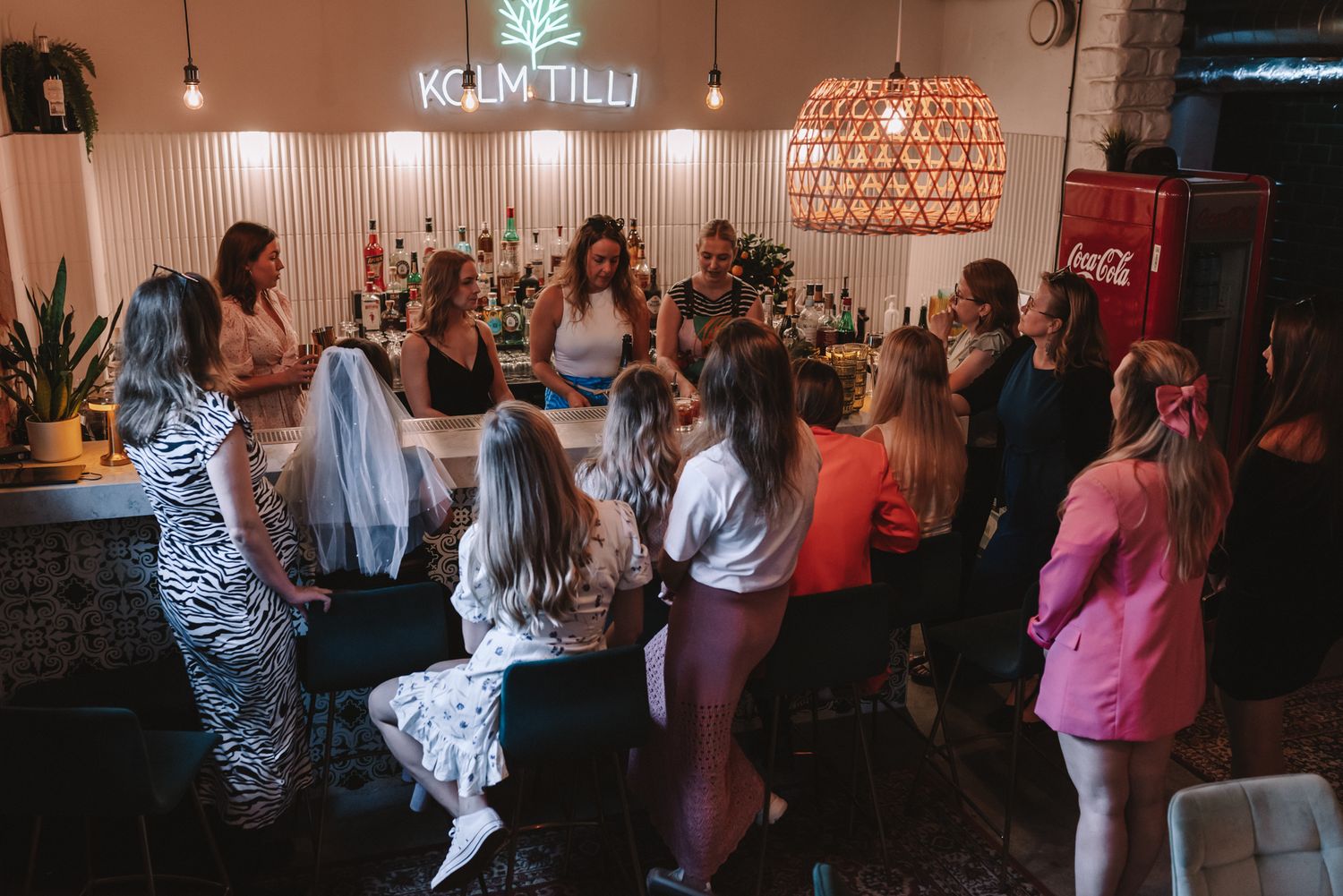 A lively group gathers at a bar or event space with modern lighting fixtures and decor during a social gathering.