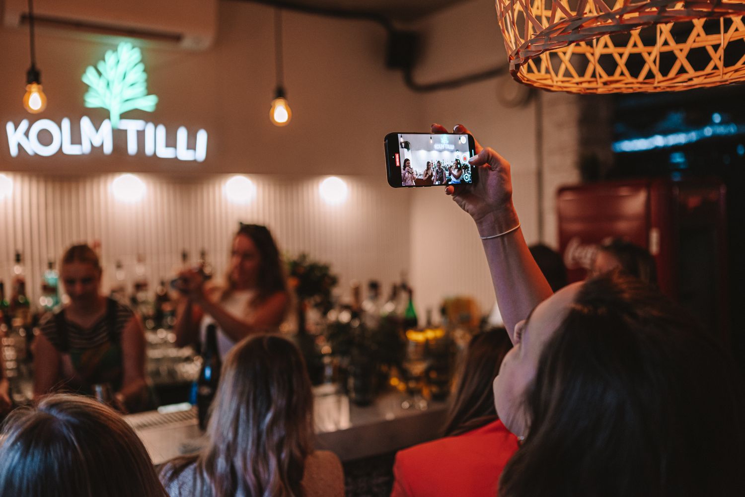 Person holding up phone to take photo in dimly lit restaurant with illuminated Kolm Tilli sign visible on wall.