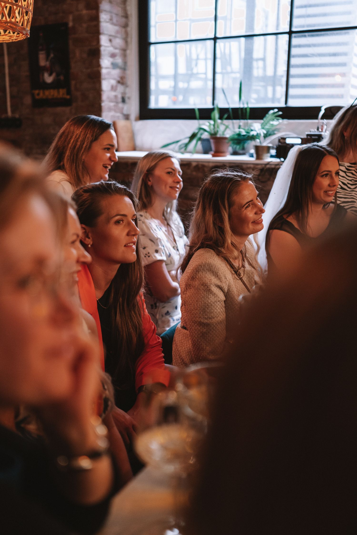 A group of people laughing and smiling together at a social gathering in a warmly lit room with brick walls.