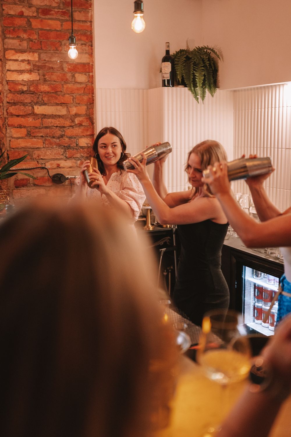 People enjoying drinks at a bar with exposed brick walls and hanging light fixtures in a cozy restaurant setting.